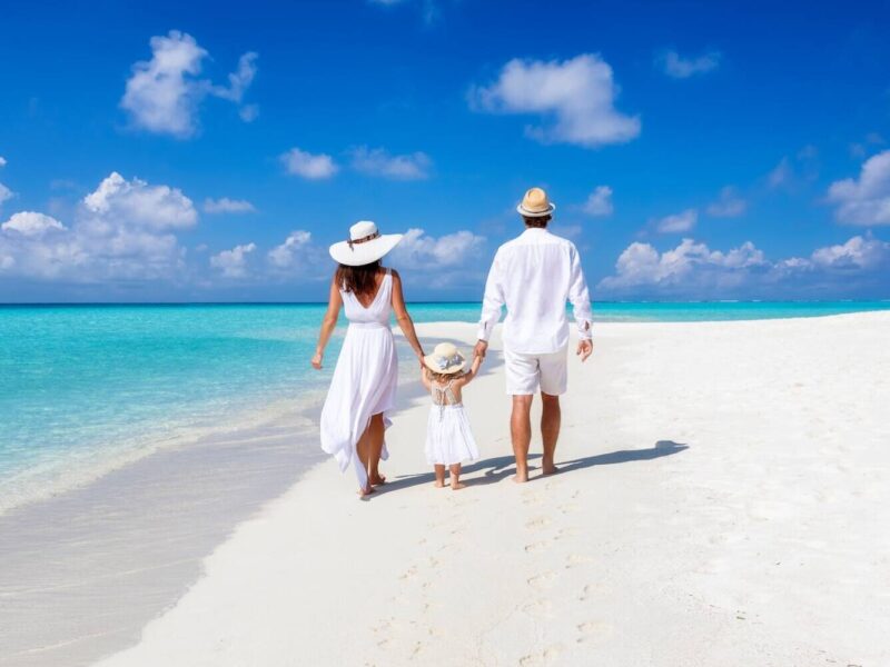 A beautiful family walks together on a tropical paradise beach in the Maldives with turquoise ocean and white sand during their vacation time