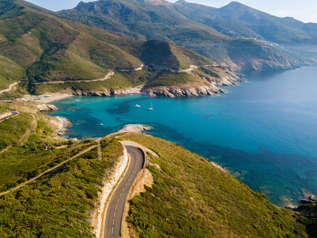 Vista aerea della costa della Corsica, strade serpeggianti e calette con mare cristallino. Penisola di Cap Corse, Corsica. Tratto di costa. Anse d'Aliso. Golfo d’Aliso. Francia